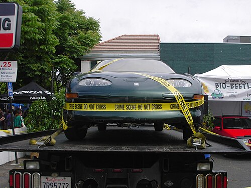 Front view of a dark green car, with yellow caution taping exclaiming, 